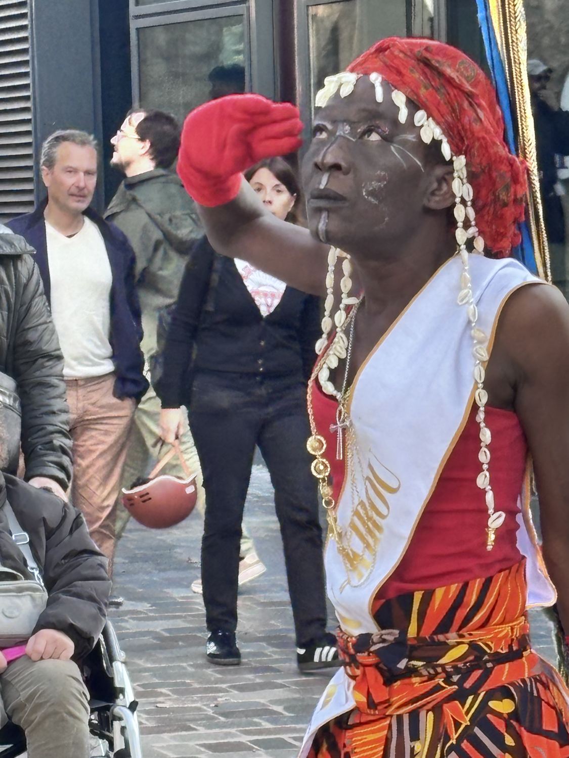 Portrait de Kemet, coiffe de cauris et gants rouges, la main levée vers le ciel